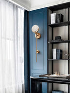 Clérachic wall sconce mounted on deep blue joinery beside a study window, its alabaster disc catching the daylight.