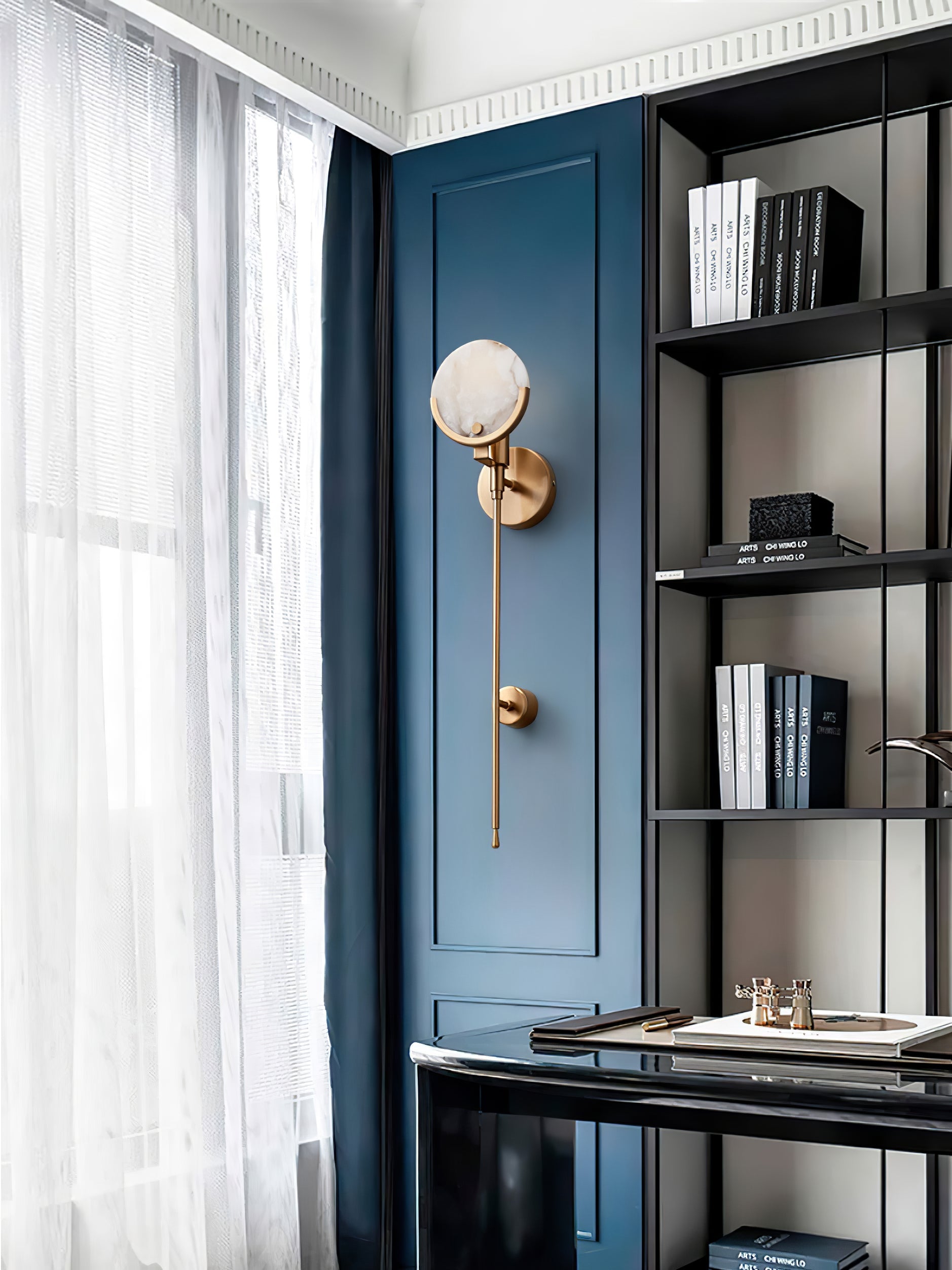 Clérachic wall sconce mounted on deep blue joinery beside a study window, its alabaster disc catching the daylight.