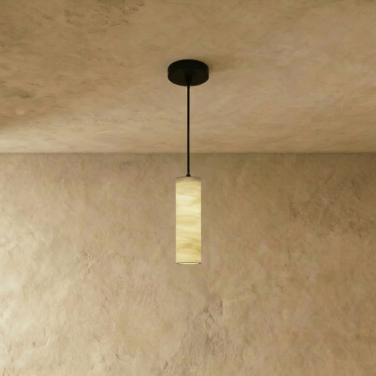Clérachic alabaster cylinder pendant with a black rod and canopy, its veined stone softly lit against a textured plaster wall.