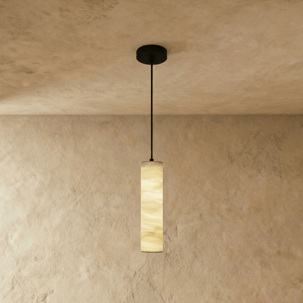 Clérachic taller alabaster cylinder pendant hung from a black cord and canopy, golden veining glowing on a plaster wall.