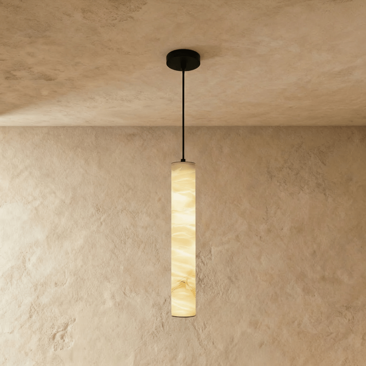 Clérachic long alabaster cylinder pendant on a thin black cord, glowing warm against a textured limewash wall and ceiling.