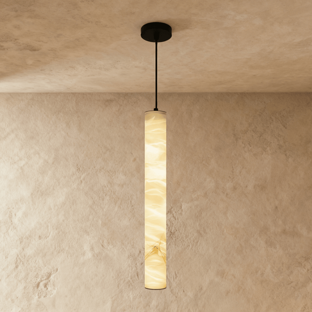 Clérachic tallest alabaster cylinder pendant on a black cord and canopy, its stone lit amber against a plaster wall.