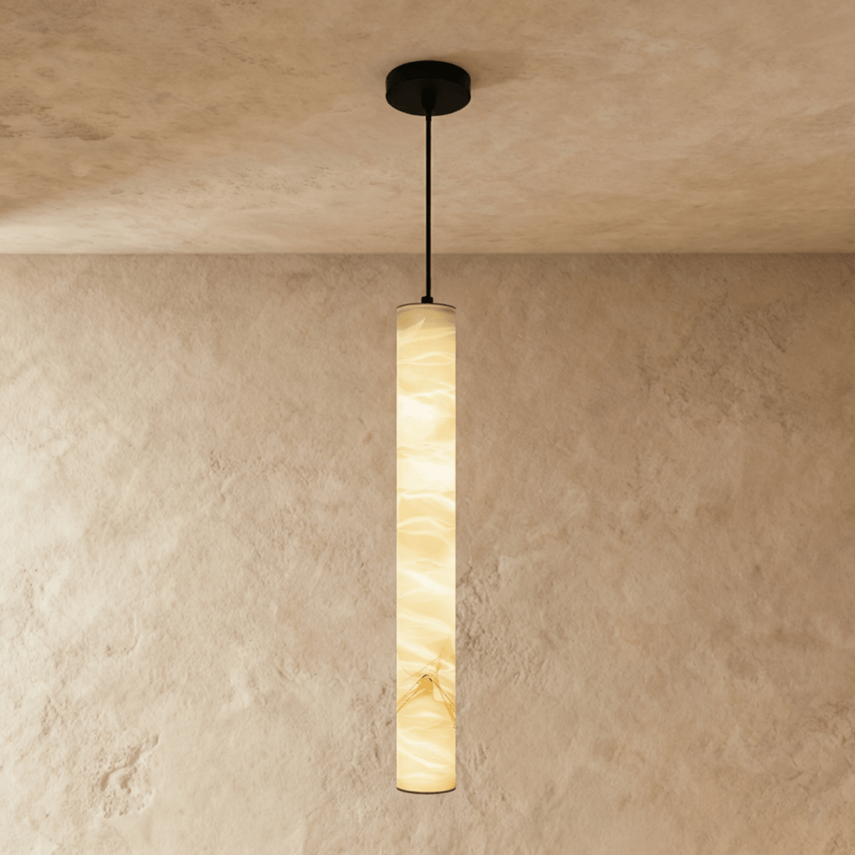 Clérachic tallest alabaster cylinder pendant on a black cord and canopy, its stone lit amber against a plaster wall.