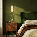Clérachic alabaster cylinder pendant hanging beside a walnut bedside cabinet and green velvet headboard, with calla lilies.