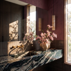 Two unlit Clérachic alabaster cylinder pendants against a plum plaster wall above a dark marble basin and pink blossom.