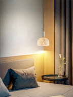 Clérachic Long-Drop Dome pendant light beside a bed, warm light spilling down a wood panel onto the bedside table.