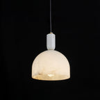 Clérachic Long-Drop Dome pendant light lit against black, the open underside pooling warm light around the bulb.