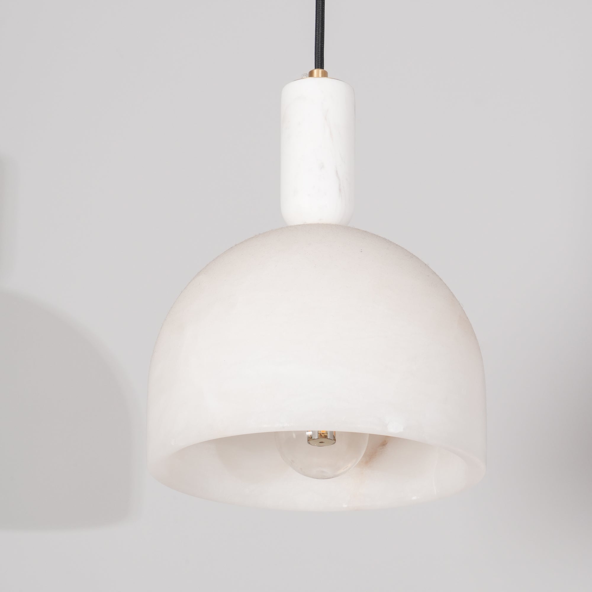 Close view of the Clérachic Long-Drop Dome pendant light, pale stone stem and brass ring above the carved dome.
