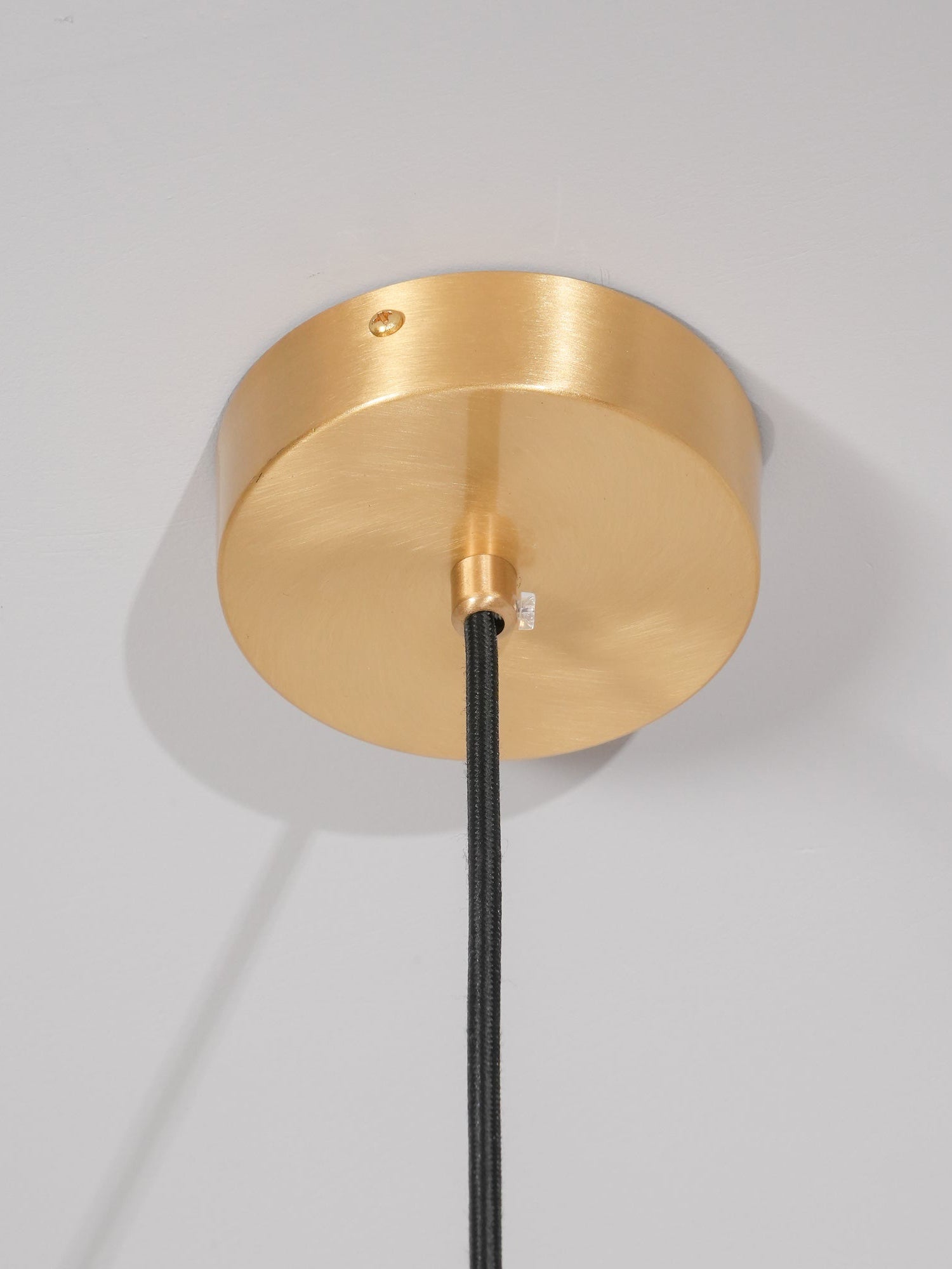The round brushed brass ceiling canopy of the Clérachic Long-Drop Dome pendant light, black braided cord below.
