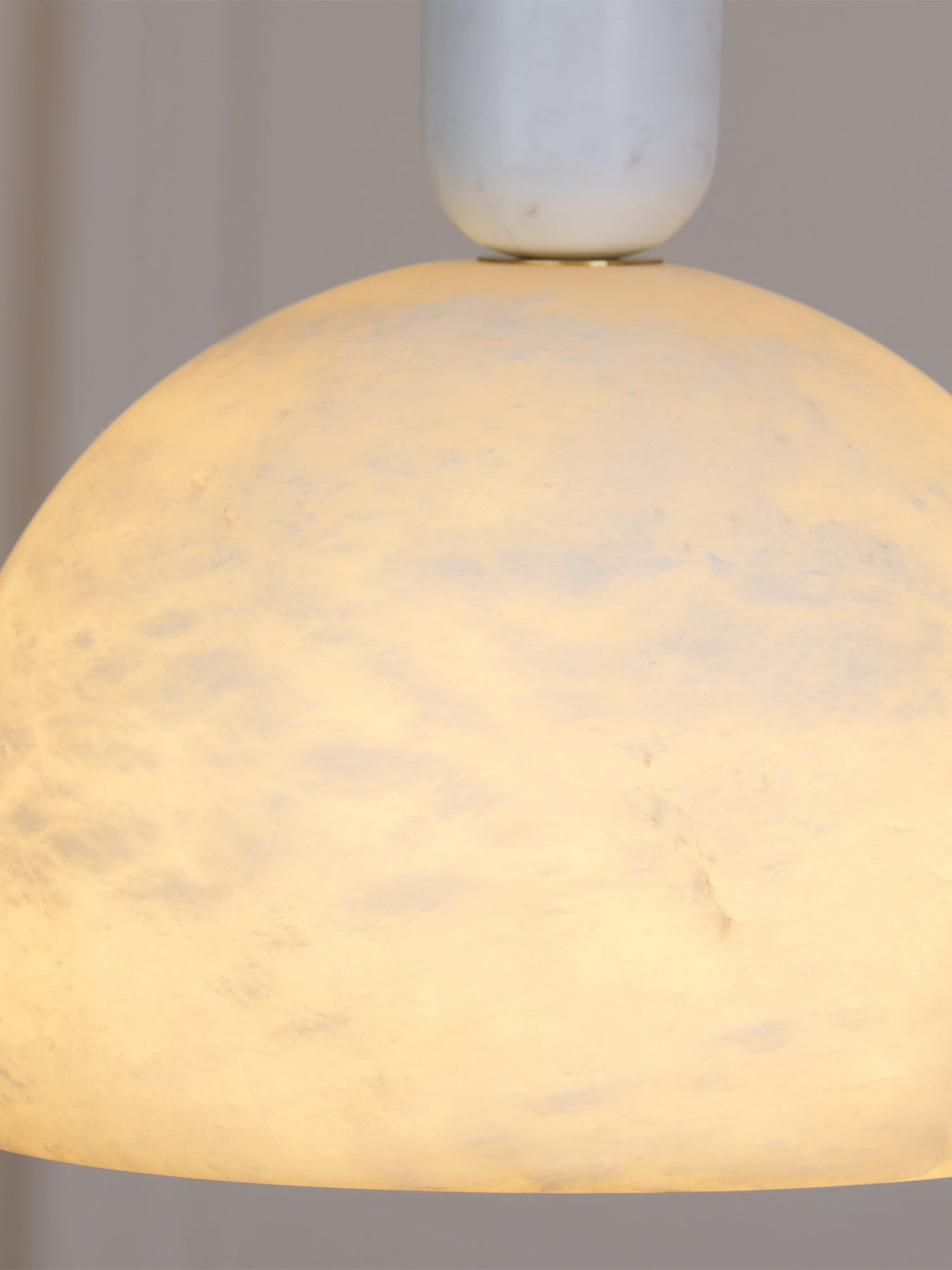 Close crop of the lit Clérachic Long-Drop Dome pendant light, warm amber light moving through the stone.