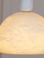 Close crop of the lit Clérachic Long-Drop Dome pendant light, warm amber light moving through the stone.