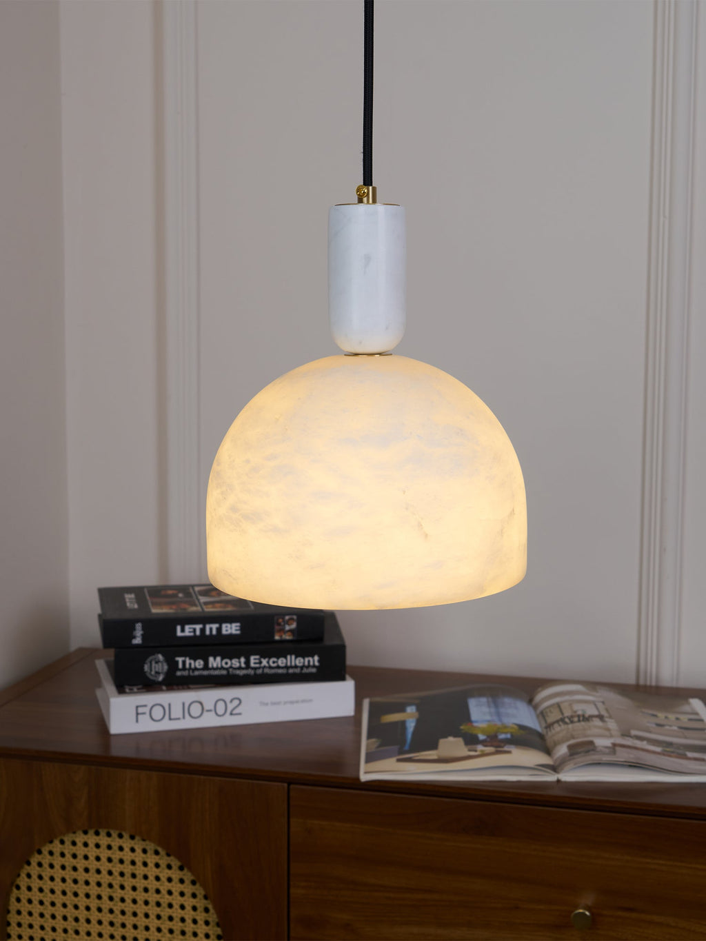 Clérachic Long-Drop Dome pendant light lit above a walnut sideboard stacked with books and an open magazine.
