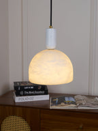 Clérachic Long-Drop Dome pendant light lit above a walnut sideboard stacked with books and an open magazine.