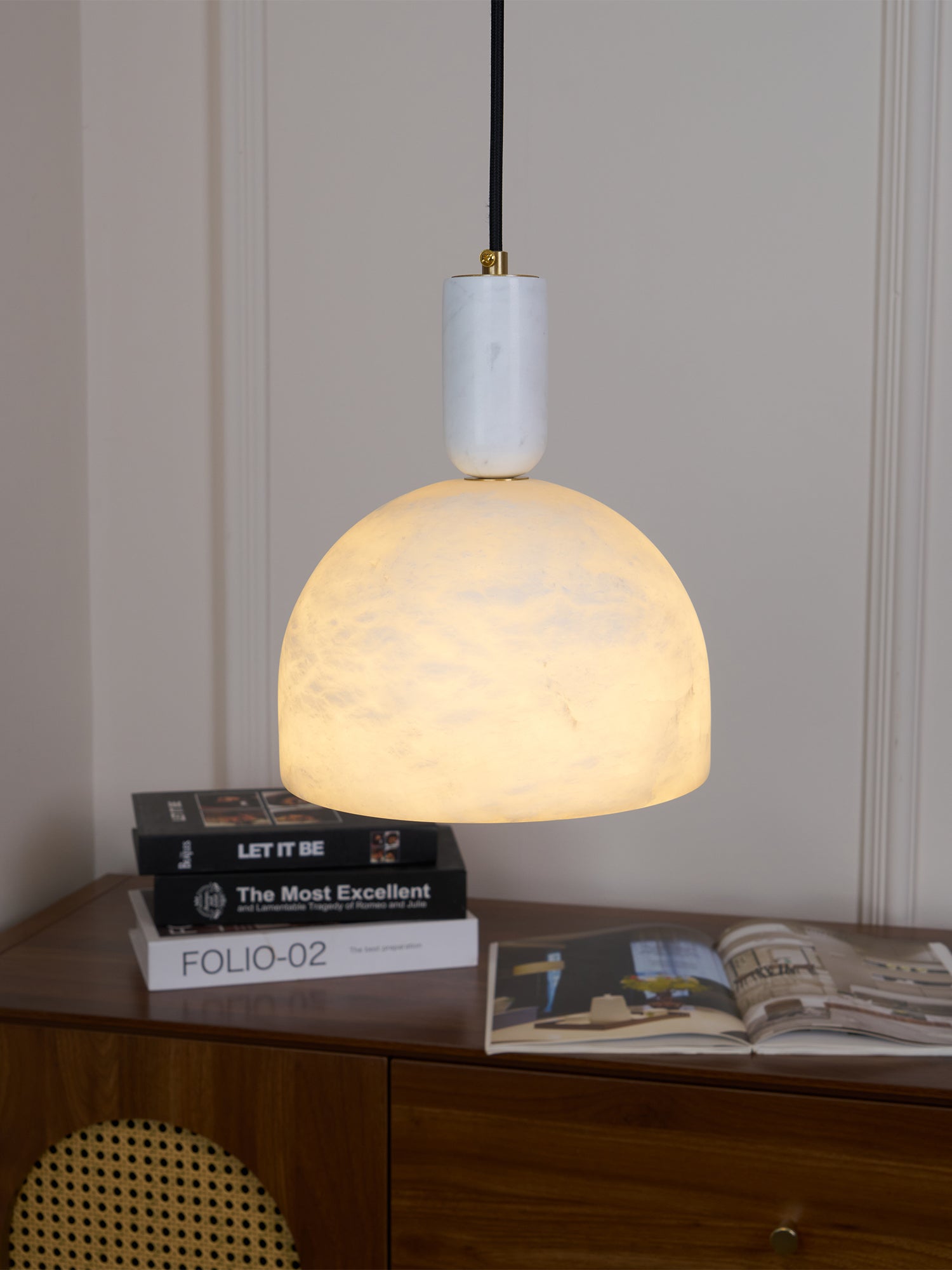 Clérachic Long-Drop Dome pendant light lit above a walnut sideboard stacked with books and an open magazine.