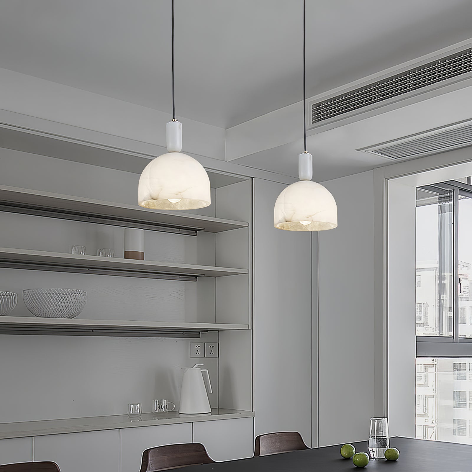 Two Clérachic Long-Drop Dome pendant lights lit over a table in a pale grey kitchen with open shelving.