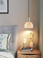 Clérachic Long-Drop Dome pendant light as bedside lighting, warm light falling over eucalyptus on a wood nightstand.