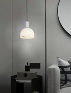 Clérachic Long-Drop Dome pendant light lit beside a black side table and a round mirror in a grey bedroom.