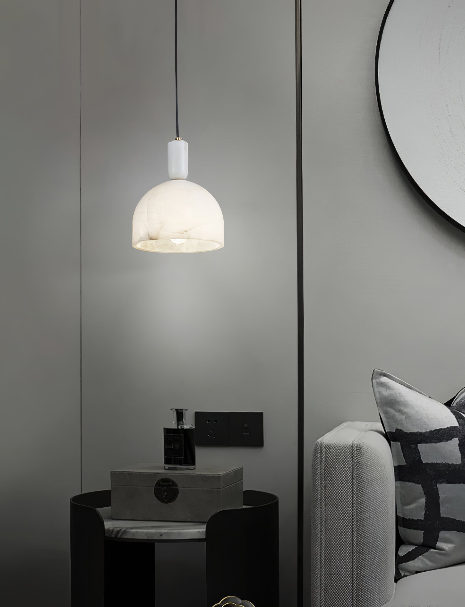 Clérachic Long-Drop Dome pendant light lit beside a black side table and a round mirror in a grey bedroom.