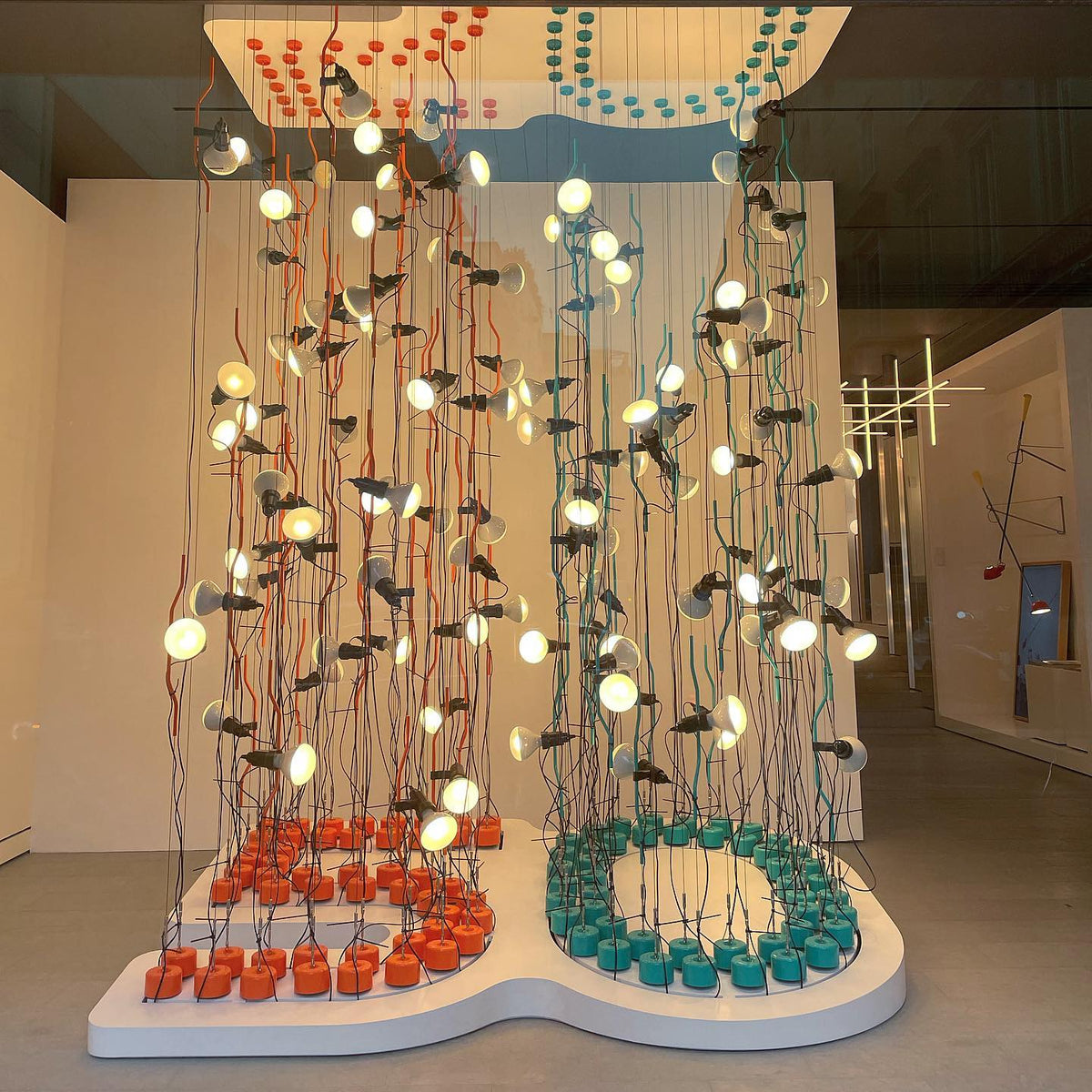 Large installation of many Clérachic spotlight pendants hanging in rows from red and teal cords above round coloured bases.
