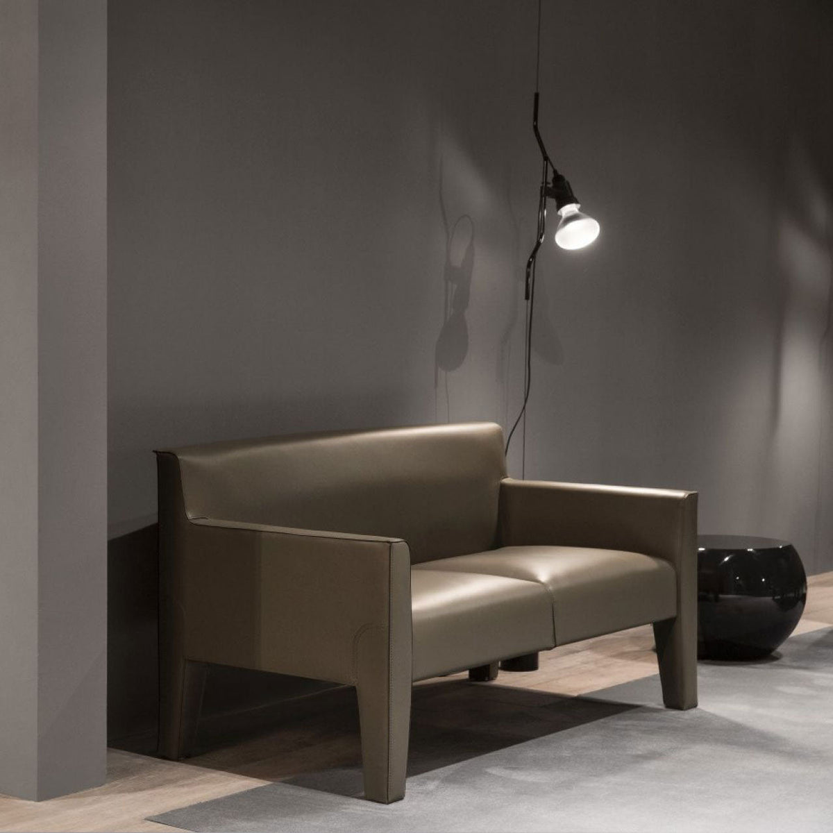 Lit Clérachic pendant spotlight on a long cable above a grey-green leather sofa in a dark grey room.