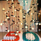 Close view of many Clérachic spotlight pendants lit among red and teal cords, hanging above round coloured bases.