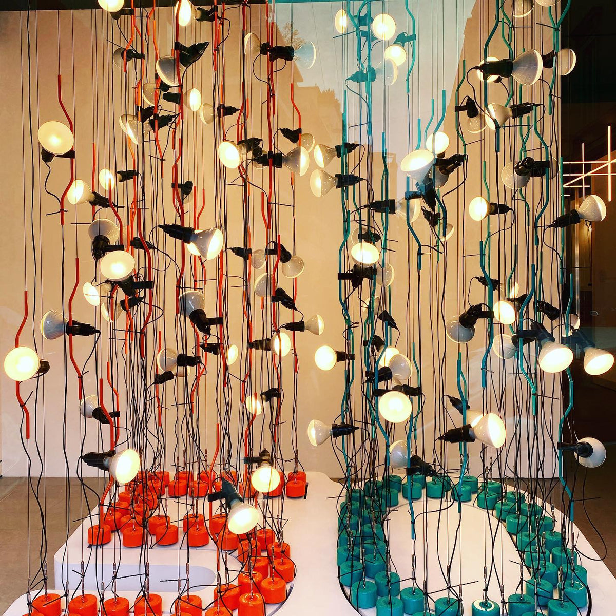 Close view of many Clérachic spotlight pendants lit among red and teal cords, hanging above round coloured bases.