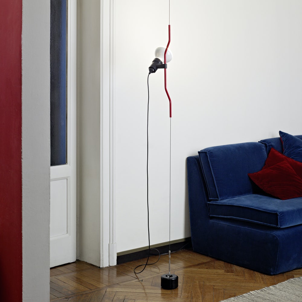 Clérachic pendant with a red bendable cord section hanging down to a black base, in a white room beside a blue velvet sofa.