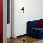 Clérachic pendant with a red bendable cord section hanging down to a black base, in a white room beside a blue velvet sofa.