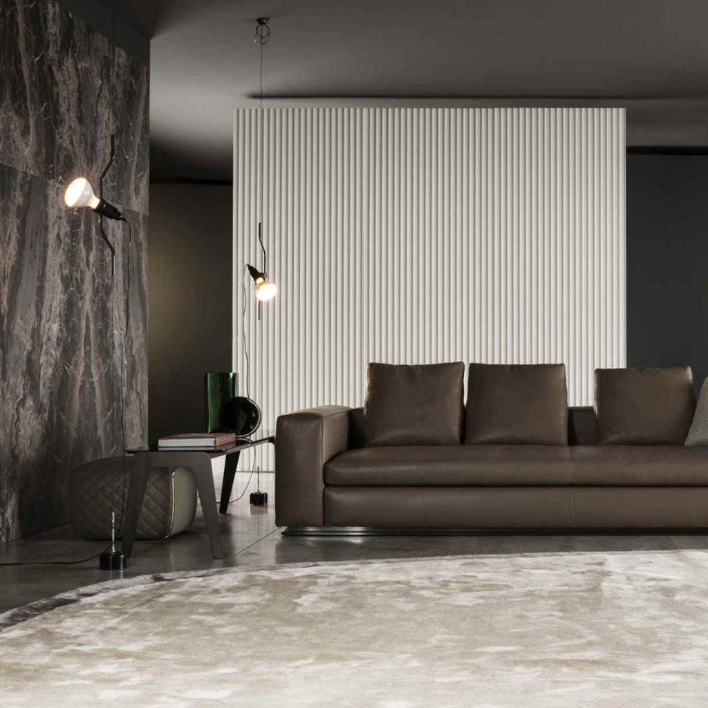 A Clérachic pendant spotlight lit against a dark stone wall, with a brown leather sofa and a ribbed white panel beyond.