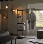 Clérachic pendant spotlights lit on cables beside a black clothes rail, a bench and a window with a green view.