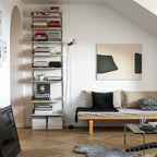 A Clérachic pendant spotlight hanging beside a tall bookshelf, above a daybed with cushions and a sheepskin rug.