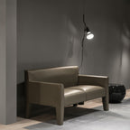 Lit Clérachic pendant spotlight above a green-grey leather sofa and a black side table, against a grey wall.