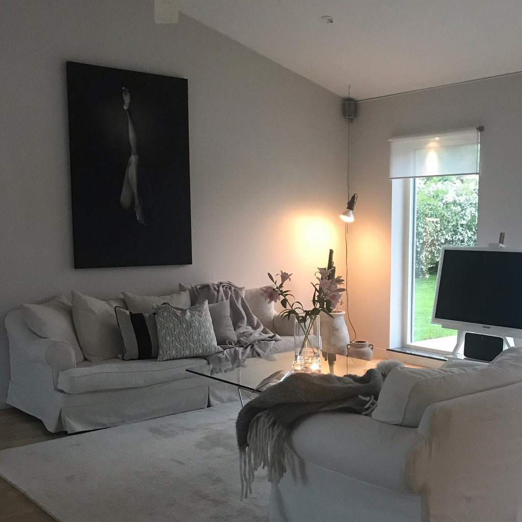 A Clérachic pendant spotlight lit in a living room with a white sofa, a glass table and a framed black and white portrait.