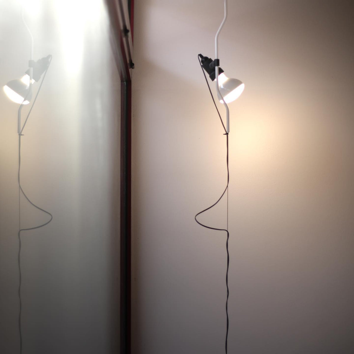 Two lit Clérachic pendant spotlights on thin cables, one in front of a wall and one beside a doorway, with long loops of cord.