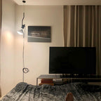 A Clérachic pendant spotlight with a white bulb hanging beside curtains, above a low table and a television, with the cable looped on the floor.
