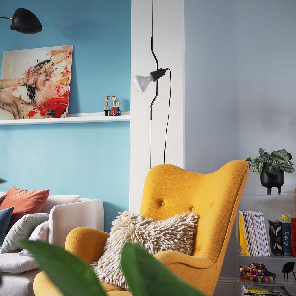 Clérachic pendant spotlight with a white bulb above a yellow armchair, in a room with a sky-blue wall and a colourful print.