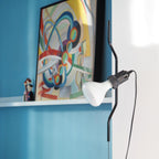 Close view of a Clérachic pendant with a black bendable cord and a white bulb in a black socket, against a blue wall.