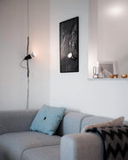 Clérachic pendant spotlight beside a framed black print, above a pale grey sofa with a blue cushion and a patterned throw.