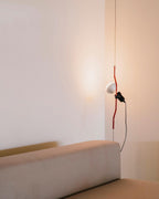 A Clérachic pendant with a red bendable cord section and a white bulb, hanging in a corner above a beige sofa.