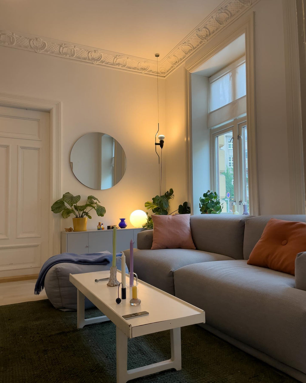 Clérachic pendant spotlight hanging by a tall window in a living room with a grey sofa, a round mirror and a white coffee table.