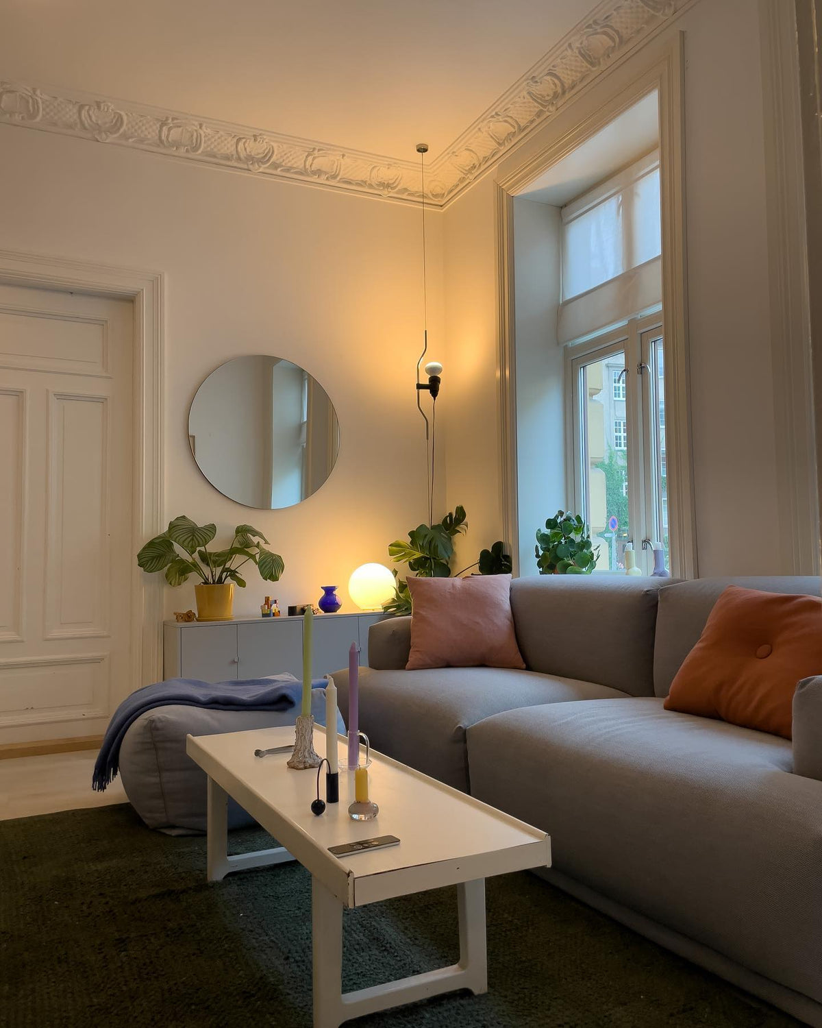 Clérachic pendant spotlight hanging by a tall window in a living room with a grey sofa, a round mirror and a white coffee table.