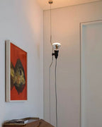 A Clérachic pendant spotlight lit beside a door, with a red-toned painting on the wall and a small desk below.