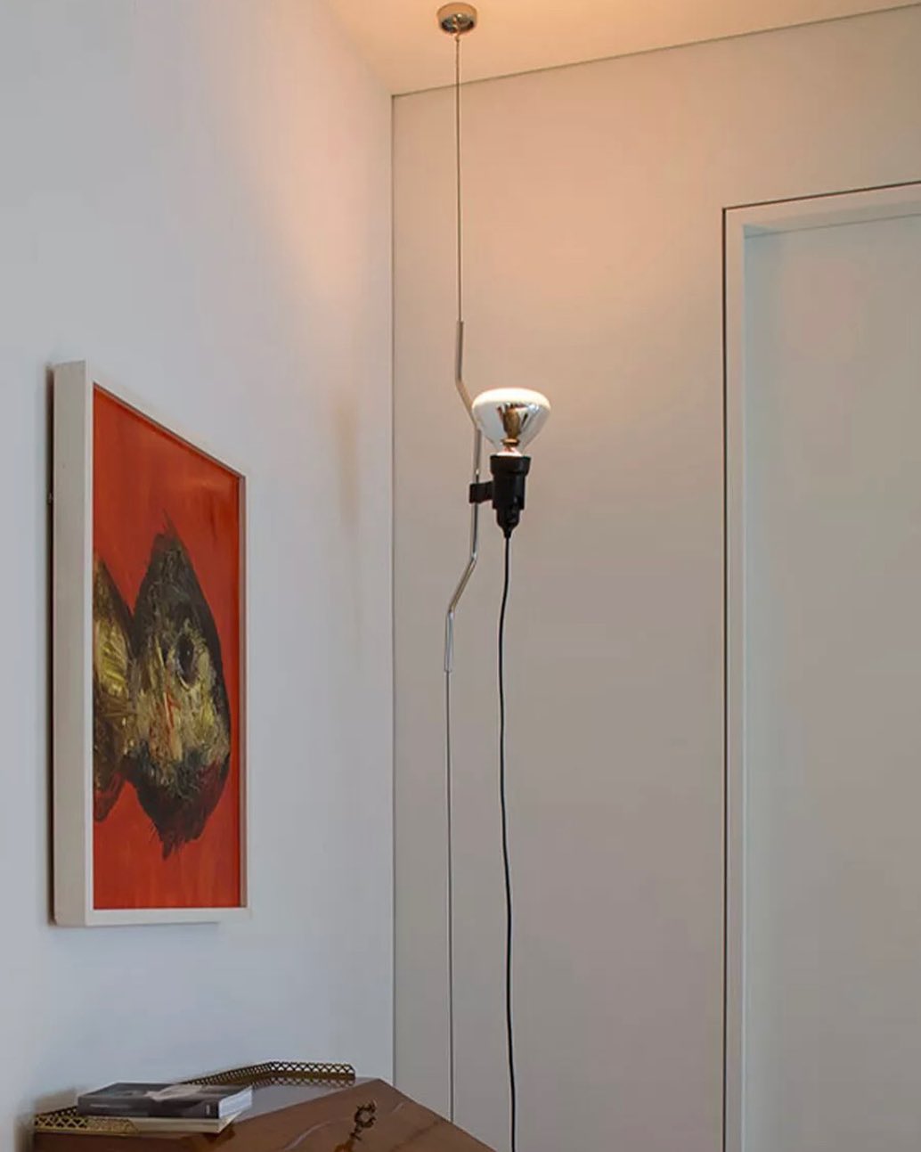 A Clérachic pendant spotlight lit beside a door, with a red-toned painting on the wall and a small desk below.