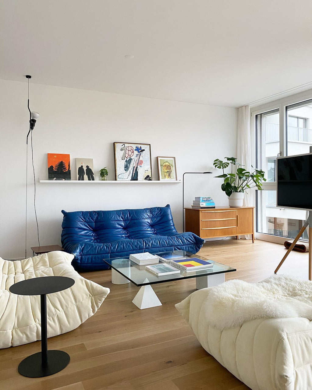 A Clérachic pendant spotlight on a thin cable in a bright living room with a blue leather sofa, a glass table and white lounge seating.