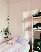 A Clérachic pendant with a black bendable cord and a small spotlight in a pink-toned room, above a bed and a banana plant.