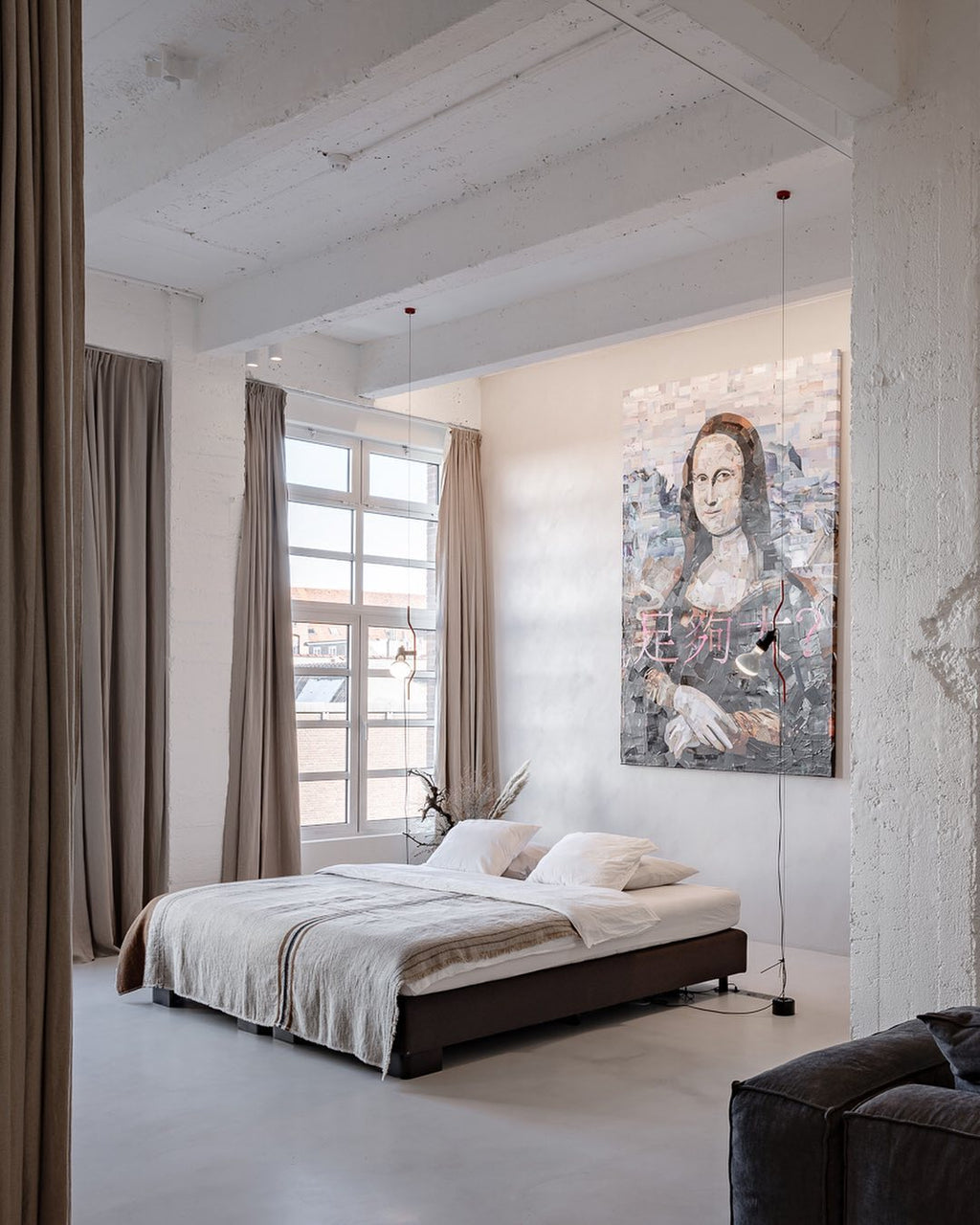 A Clérachic pendant on a long cable in a large white room with a low bed, a tall window and a painted portrait on the wall.