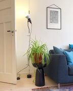 A Clérachic pendant spotlight lit above a spider plant on a dark pedestal, beside a navy sofa and a white door.