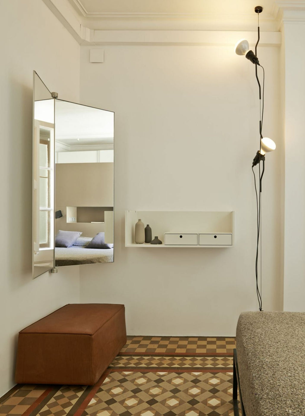 Two Clérachic pendant spotlights hanging on cables in a narrow room with a tiled floor, a tall mirror and a tan leather bench.