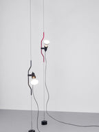 Two Clérachic pendants, one with a red bendable cord section and one in black, hanging side by side on cables against a plain wall.