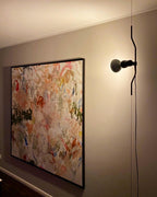 A Clérachic pendant with a black bulb housing on a bendable cord, hanging beside a large abstract painting on a taupe wall.